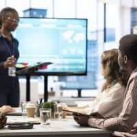 Coworkers engaging in a problem solving meeting at a corporation, using an interactive board to visualize data and develop solutions for complex business challenges. Analysis presentation.